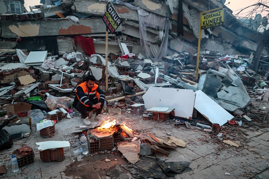 Un hombre trata de calentarse en una hoguera encendia en medio de los escombros de un edificio derrumbado en Hatay, tras el terremoto del lunes en Turquía.